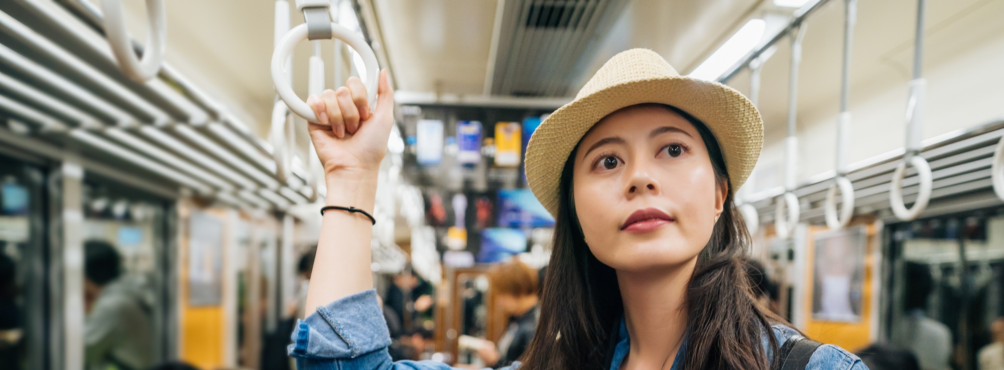 Young woman in straw fedora hat standing on subway holding a ceiling bar