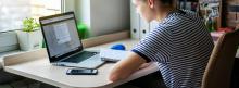 Woman sitting at home by her desk with laptop and notebook